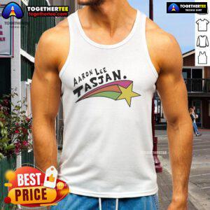 Happy Aaron Lee Tasjan wearing a colorful rainbow star tank top, radiating joy and style at a vibrant outdoor event.