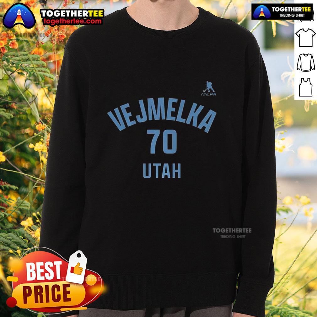 Alt Text: Happy Karel Vejmelka wearing a Utah Mammoth ice hockey sweatshirt with the name and number 70, smiling outdoors.