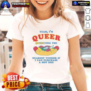 Queer person in a 'Nice Yeah I'm Queer' tee, querying a vendor for a hot dog at a lively street fair.