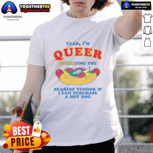Person in a 'Nice Yeah Im Queer' shirt asking a vendor about purchasing a hot dog t-shirt at a street fair.